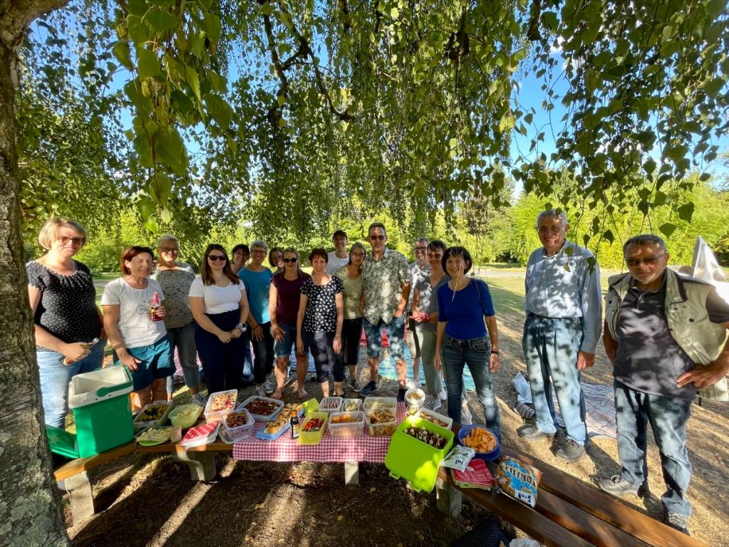 unCHORRekt_Picknick in der Gruga_komprjpeg Die Chormitglieder von unCHORrekt stehen am Picknickbuffet unter einer großen Birke